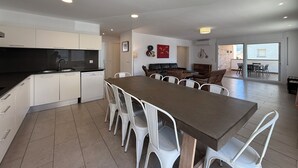 Une cuisine moderne avec des meubles blancs, un coin repas avec une longue table et des chaises blanches, et un espace de vie agrémenté d’un canapé et d’une décoration sur le thème du vélo.