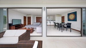 A modern living room with a sofa, television, and a dining area with a table and chairs. - Tranquil Residence 3 (Koh Samui)