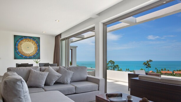 A modern living room with a grey sofa, a coffee table, and a large window offering a view of the ocean. - Tranquil Residence 3 (Koh Samui)