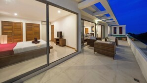 A modern bedroom with a large sliding glass door, a bed, a TV, and a seating area with wicker furniture. - Tranquil Residence 3 (Koh Samui)