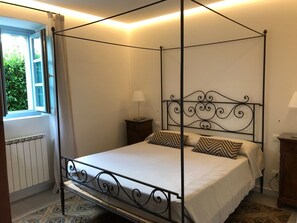 Relax in this serene space with a four-poster bed and a bedside table, offering a peaceful view of the surrounding greenery.