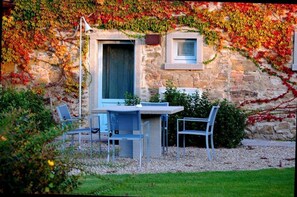 Sit and enjoy the view from this charming outdoor seating area, adjacent to the building with a large window and a smaller window.