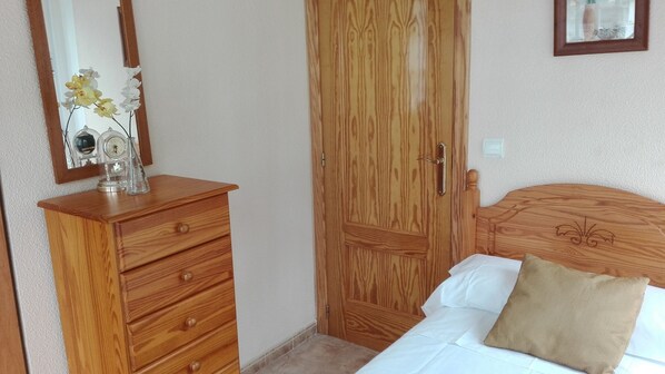 Een slaapkamer met een houten dressoir, een bed met hoofdeinde en een houten deur.