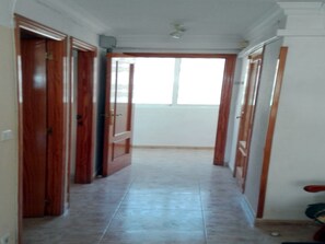 Un pasillo con puertas de madera que dan a habitaciones, piso de baldosas y un ventanal al final.