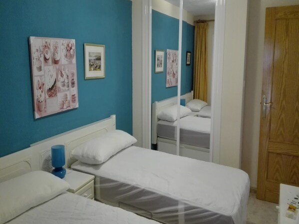 Una habitación con dos camas, una pared azul y una puerta de madera.