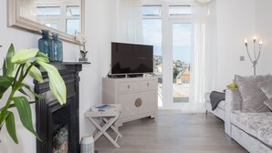 Een moderne woonkamer met een flatscreen televisie, een witte bank, een open haard en een groot raam met uitzicht op gebouwen.