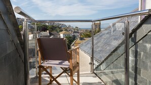 Een balkon met helder uitzicht over de stad, een houten stoel en een glazen hekwerk.