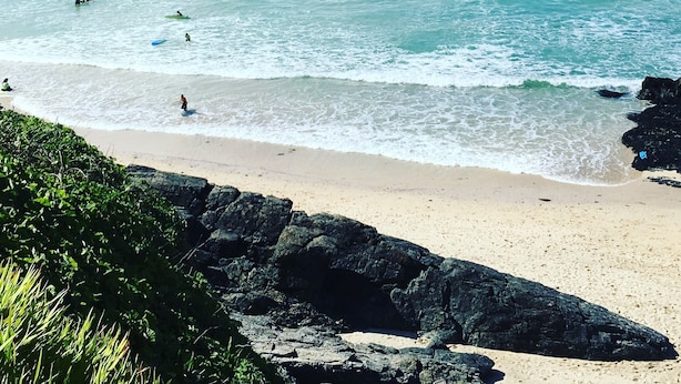 Een strand met helder turquoise water, golven en een rotsachtige kustlijn.