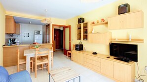 A compact living space with a kitchenette, dining area, and entertainment unit. - PUIG ROM 115 1 2  Roses (Rosas / Roses)