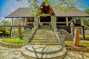 A building with a stone staircase leading to a wooden door, surrounded by greenery and stone walls.