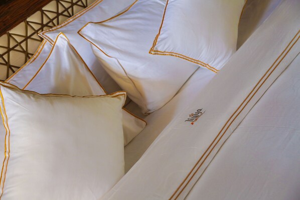 Una cama con sábanas blancas y adornos dorados, cabecera de madera y pared con un estampado geométrico.