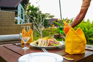 A dining table with a plate of food, a glass of water, and a cocktail.