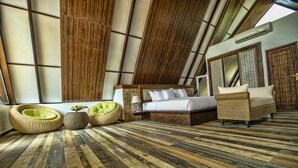 Una habitación con techos altos y techo inclinado, una cama grande, dos sofás de mimbre y una zona de estar con un sillón redondo.