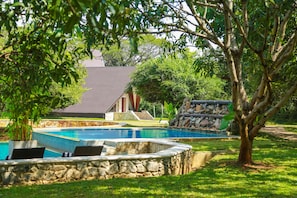 A swimming pool with stone borders, a stone wall, and a tree in the foreground.