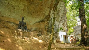 Una cueva con una estatua sentada, un edificio pequeño y un árbol.
