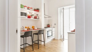 A modern kitchen with white cabinetry, a built-in oven, and a countertop with a kettle and orange juice. There are two black bar stools and a red mat on the counter. - Central, next to the Metro, overlooking the famous Appia Antica Park (Roma)