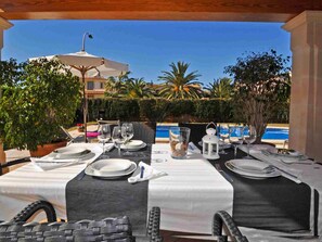 Zona de menjador a l'aire lliure amb taules preparades per a dues persones, amb vista a una piscina.