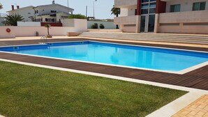 Piscina retangular com deck de madeira e área gramada em primeiro plano.