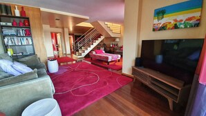Uma sala de estar com sofá, televisão, escada e estante de livros.