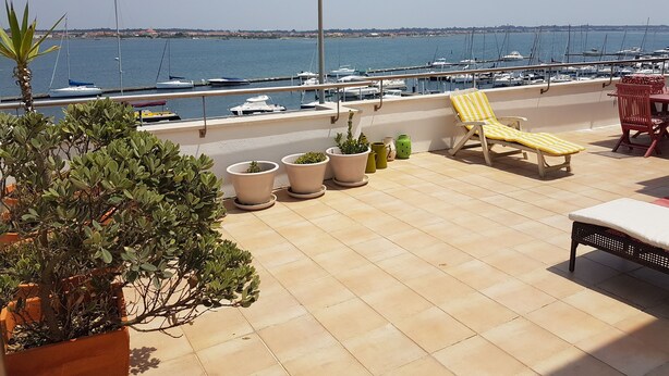Terraço com plantas em vasos, uma poltrona de lounge listrada em amarelo e uma mesa com almofada branca.