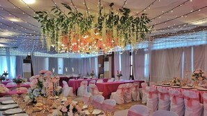 Une salle de banquet avec des tables rondes, des chaises roses et blanches, et des centres de table floraux.