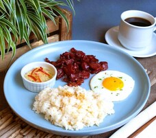 Un plato con arroz, un huevo frito, un recipiente pequeño de vegetales encurtidos y una porción de frutas rojas, acompañado de una taza de café.
