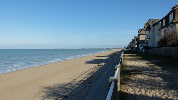 A coastal road with a sandy beach and a row of houses along the side.