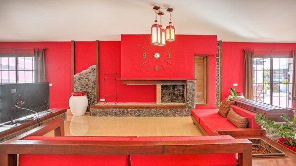 A living room with a red wall, a fireplace, a wooden bench, and a television. - Villa the path of the majorero (Antigua)