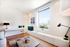Una sala de estar moderna con un ventanal grande, un televisor de pantalla plana, un banco blanco y una mesita de centro.