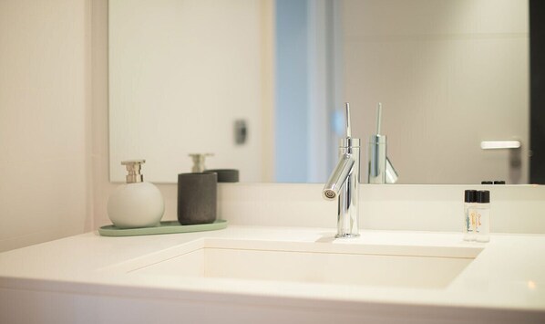 Un baño moderno con un lavabo blanco, un grifo de cromo, un espejo grande y un jabonera verde.