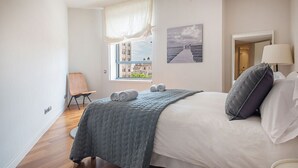 A bedroom with a bed, a window with a view, a chair, and a painting on the wall.