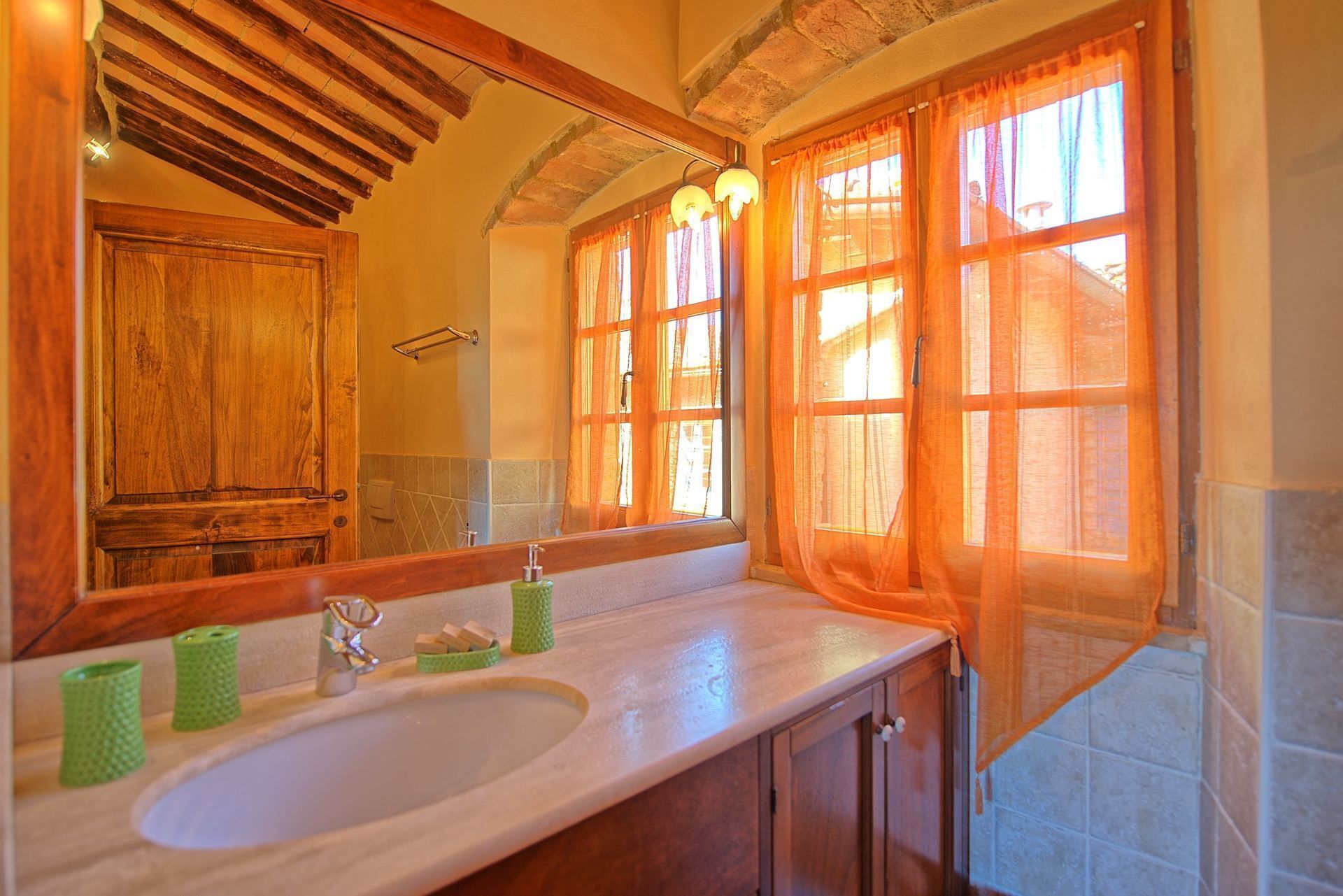 A bathroom with a wooden vanity, a large mirror, and a window with orange curtains.