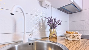 A kitchen with a stainless steel sink, a white faucet, a vase with lavender, and a basket of bread on the counter. - Split area studio apartment (Podstrana)