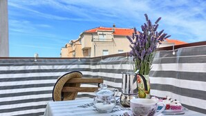 A balcony with a striped tablecloth, a wooden chair, a metal teapot, a glass sugar bowl, a cup, and a vase with lavender. - Split area studio apartment (Podstrana)