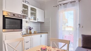 A modern kitchen with white cabinets, a built-in oven, and a dining area with a table and chairs. - Split area studio apartment (Podstrana)