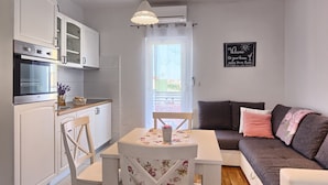 A compact kitchen with white cabinets, a dining table with chairs, and a grey sofa. - Split area studio apartment (Podstrana)