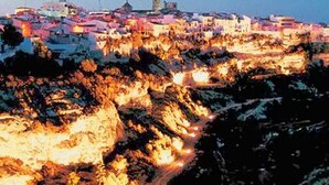 A coastal town at dusk with buildings illuminated against the sky.