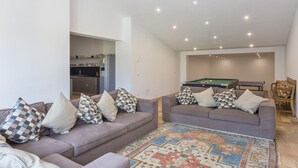 A living room with two sofas, a pool table, and a kitchen in the background.