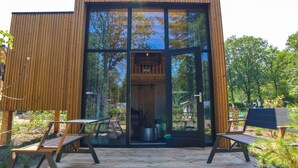 A modern wooden cabin with large glass windows, a wooden deck, and outdoor seating. - EuroParcs De Hooge Veluwe (Arnhem)