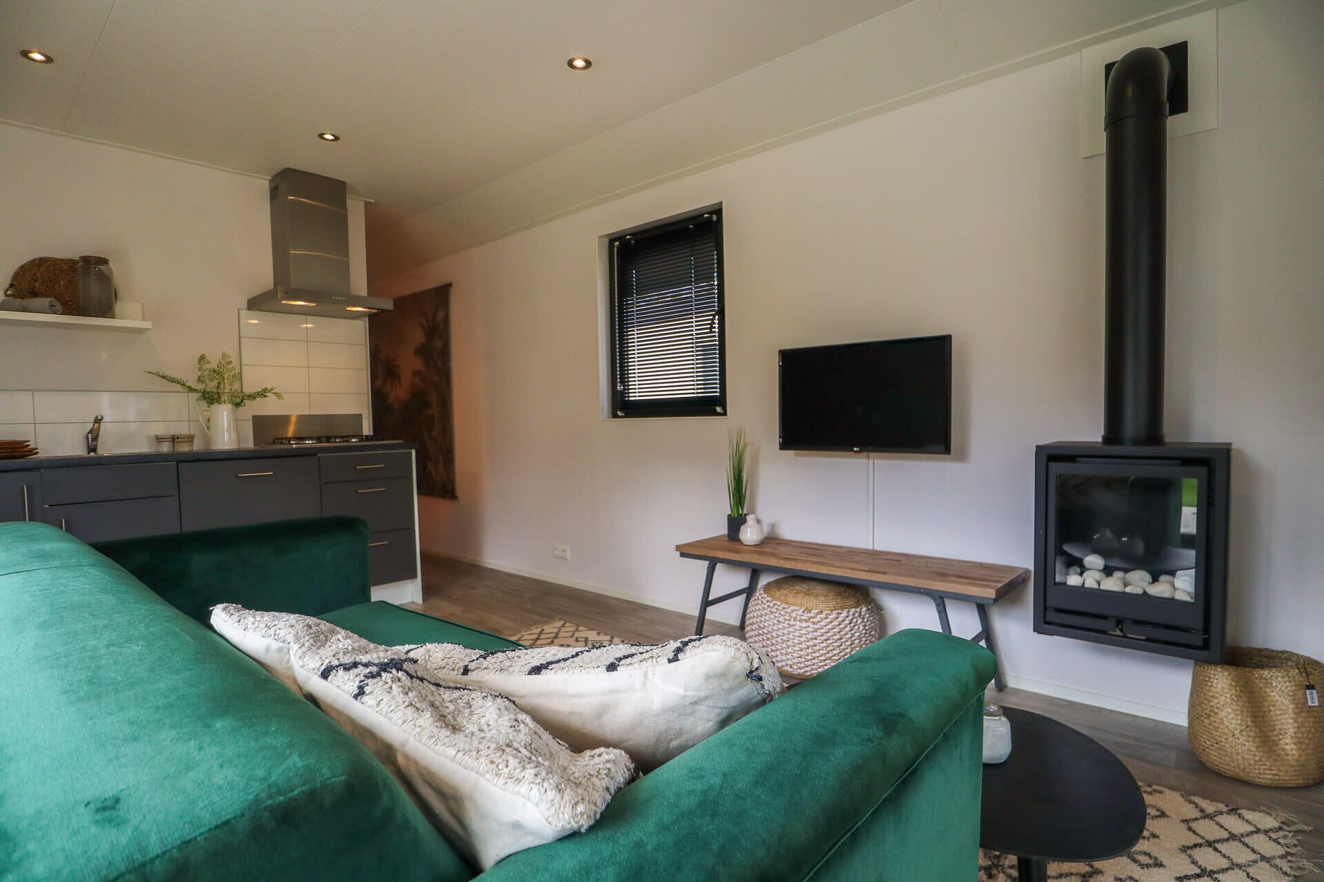 A modern living room with a green sofa, a flat-screen TV, a fireplace, and a kitchen area with white cabinets and a stove.