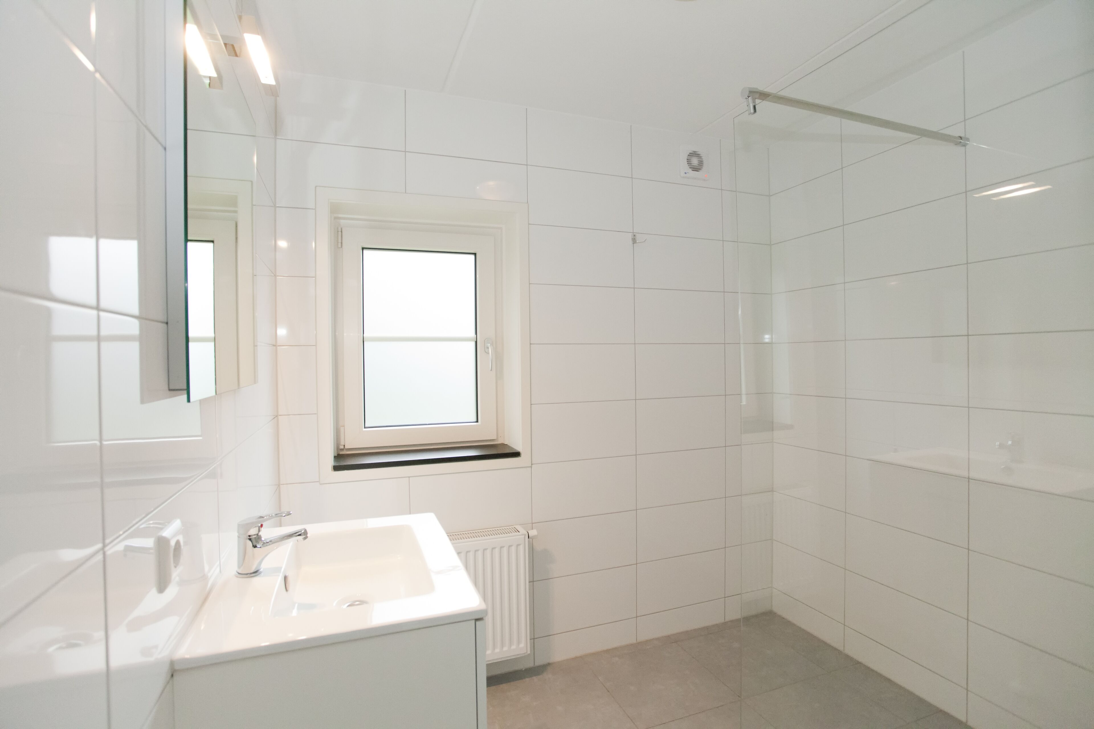 A modern bathroom with a white sink, a window, and a shower area.