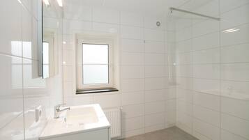 A modern bathroom with a white sink, a window, and a shower area.