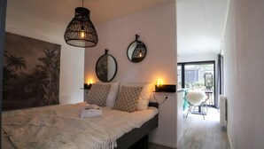 A bedroom with a bed, two wall-mounted lights, a round mirror, and a view of the outdoors. - EuroParcs De Hooge Veluwe (Arnhem)