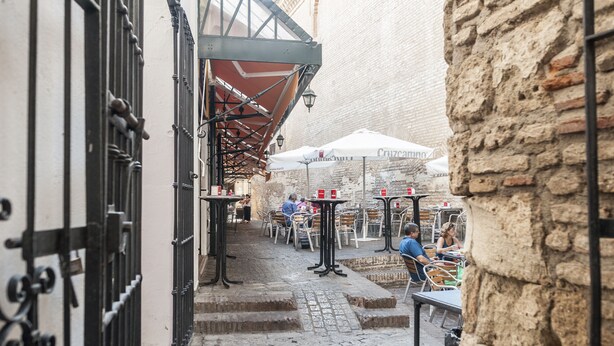 Un café en plein air avec des tables et des chaises, un mur en pierre et un portail en métal.
