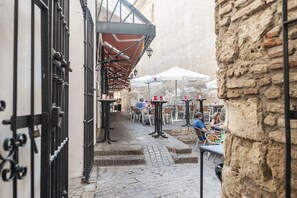 An outdoor café with tables and chairs, a stone wall, and a metal gate.