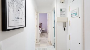 Un couloir orné d’une carte encadrée de Séville, un lit avec un mur violet et une porte avec un téléphone.