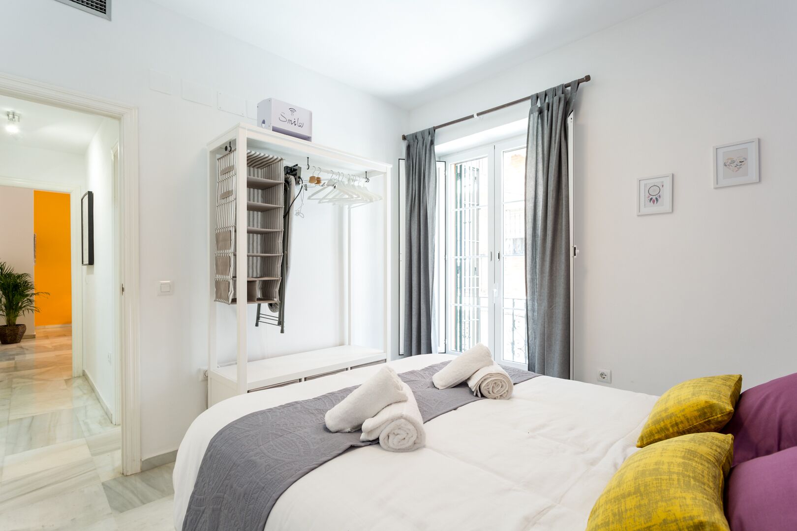 Ein Hotelzimmer mit Bett, Kleiderschrank, einem Fenster mit Vorhängen und einer kleinen Pflanze.