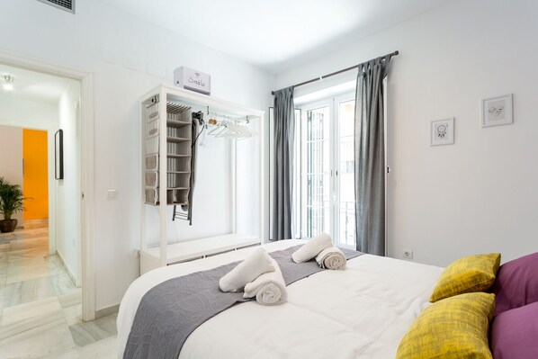 A hotel room with a bed, a wardrobe, a window with curtains, and a small plant.