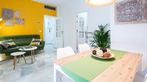 Un salon avec un canapé vert, une table basse et une table à manger agrémentée d’un chemin de table vert. Des coussins décoratifs sont posés sur le canapé et une plante en pot se trouve sur la table à manger.