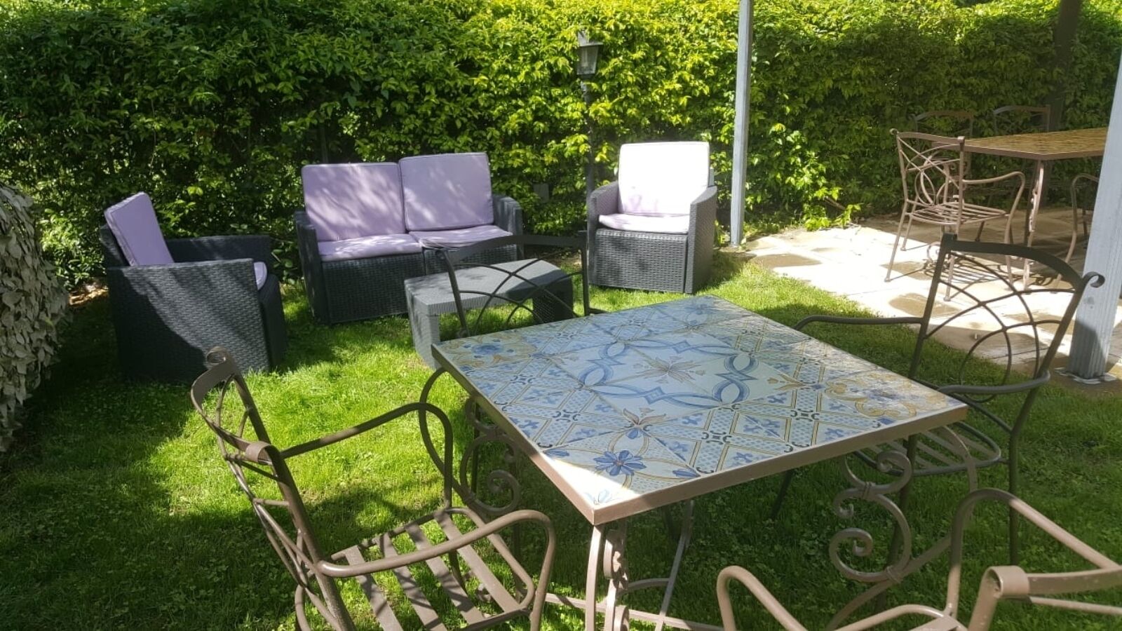 A patio with a table and chairs, surrounded by a hedge.